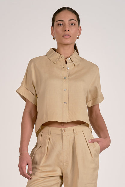 Person wearing an oatmeal short-sleeve button up shirt and pants on a plain background