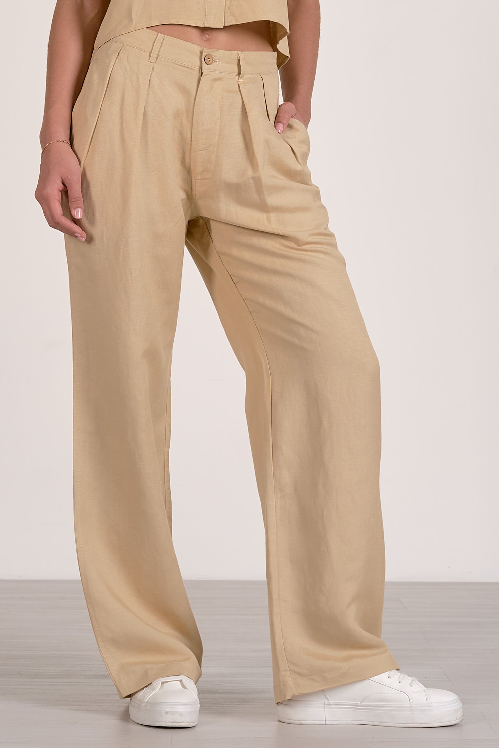 Close up Front view of woman wearing an oatmeal colored outfit with a button up shirt and oatmeal pleated pants on a plain background