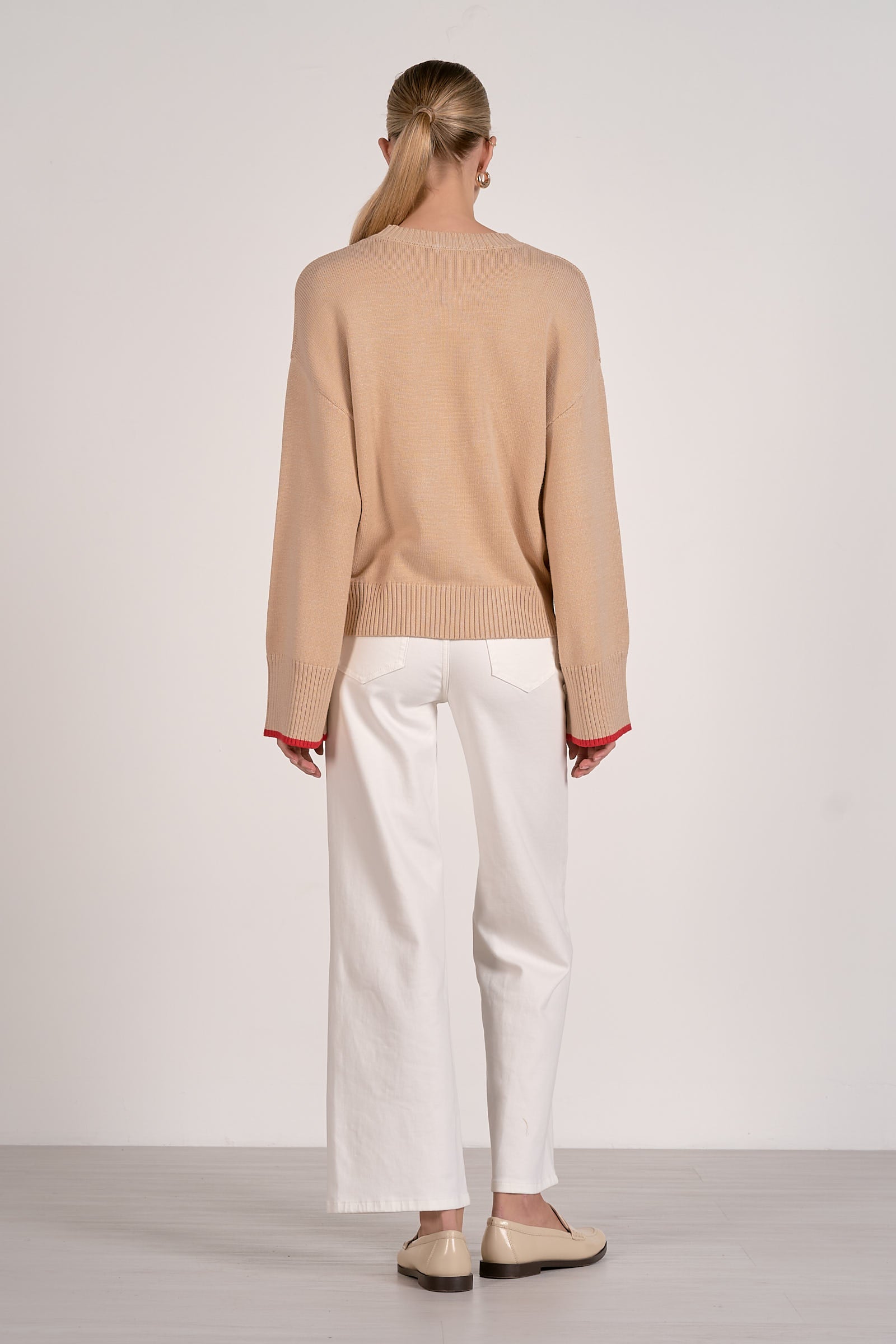 Back view of a person wearing a tan sweater and white wide leg pants on a plain background