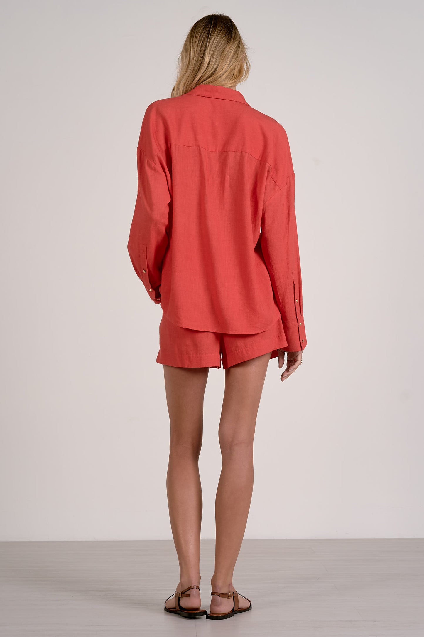 Back view of person wearing a red outfit with a shirt and shorts on a plain background