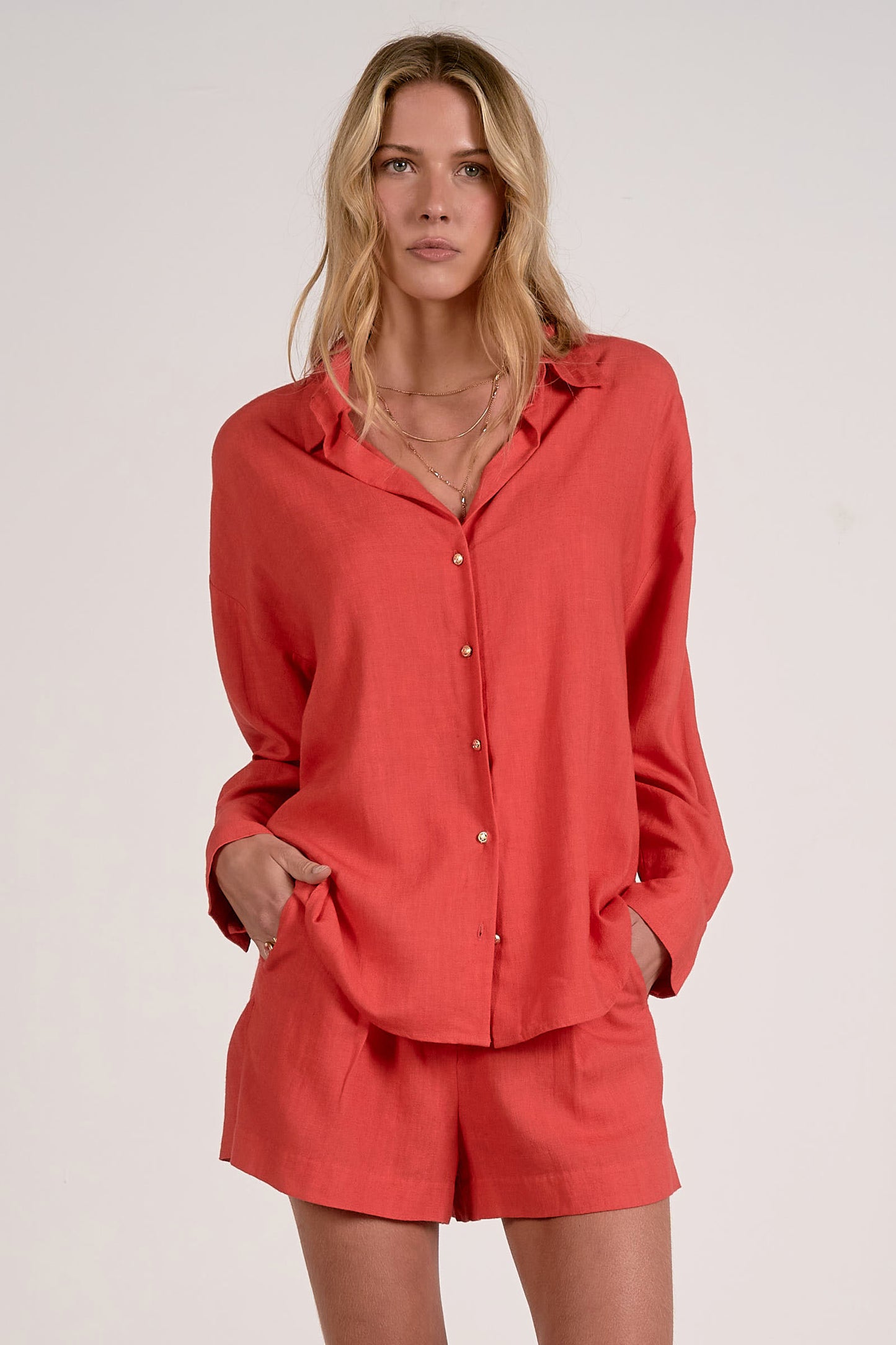 Front view of woman wearing a red button up shirt and red shorts on a white background