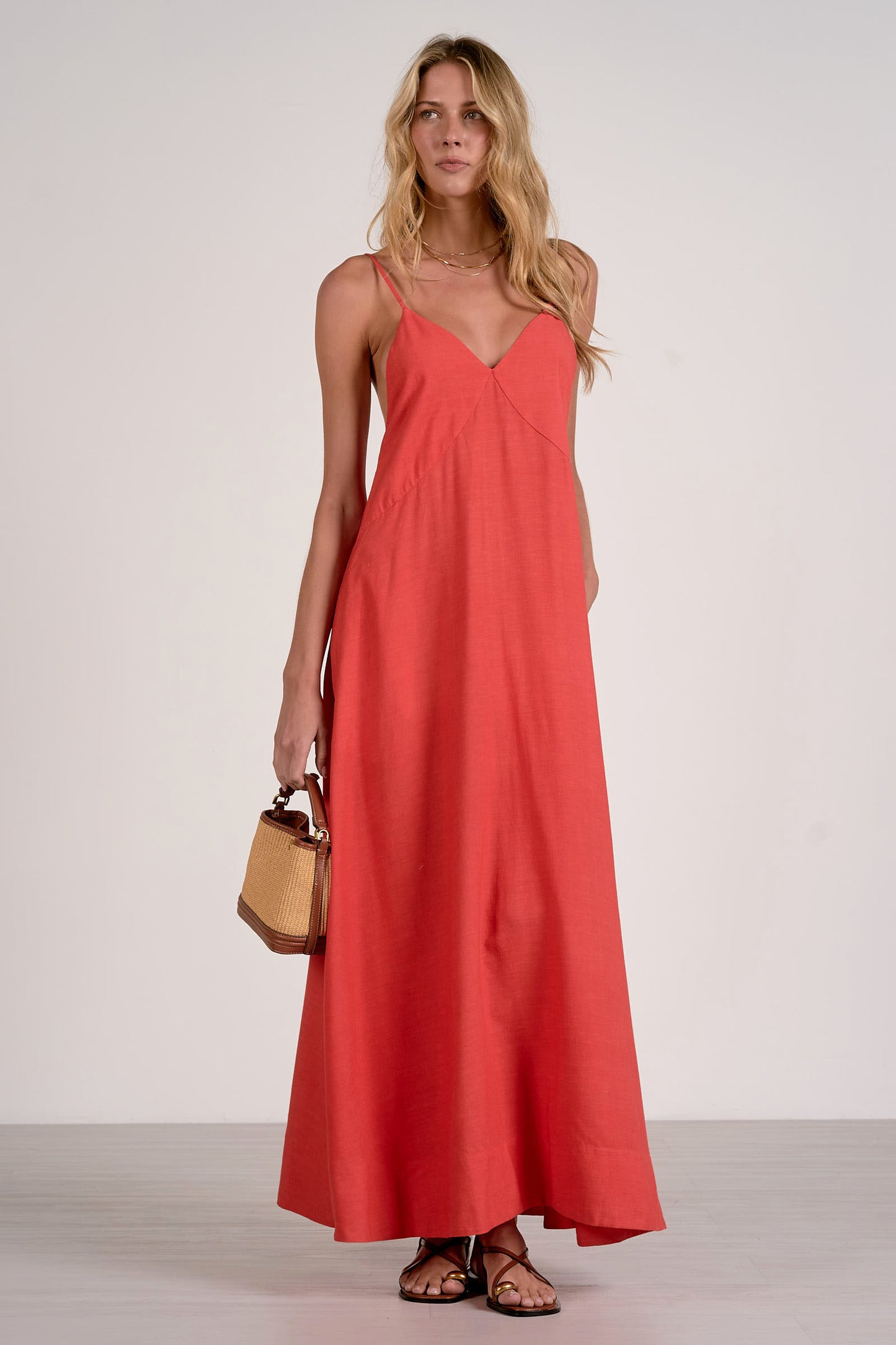 Front view of woman wearing a red v neck maxi dress holding a brown bag on a white background