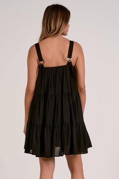 Back view of black tiered dress with tank straps worn by a model on a plain background