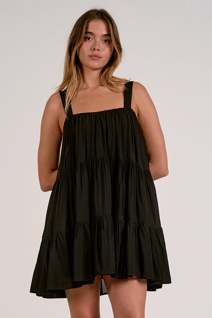 Front view of woman wearing a black tiered dress with tank straps against a plain background