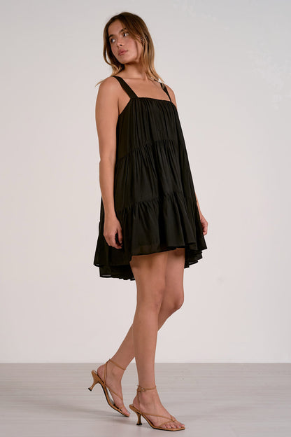 Side view of woman wearing a black tiered mini dress on a white background