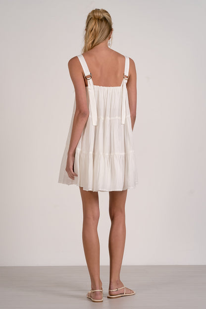 Back view of woman wearing a white tiered dress with thin straps against a plain background