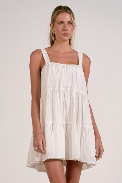 Front view of woman wearing a white tiered mini dress with tank straps against a plain background