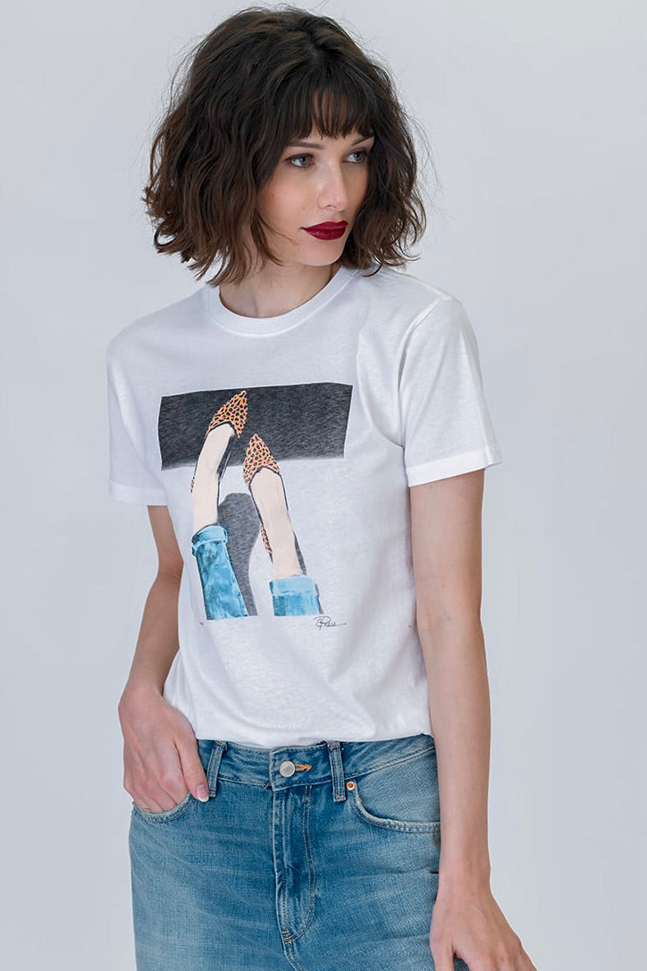 Woman wearing the 5th Ave mushie tee featuring legs and feet wearing leopard flats in white with blue jeans 