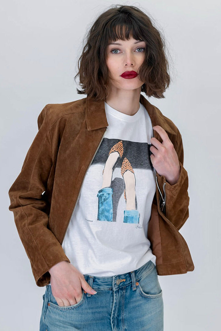 Woman wearing the 5th Ave mushie tee featuring legs and feet wearing leopard flats in white with a brown suede jacket and blue jeans 