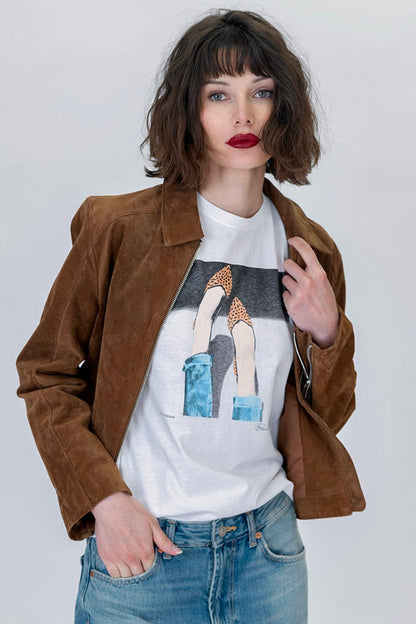 Woman wearing the 5th Ave mushie tee featuring legs and feet wearing leopard flats in white with a brown suede jacket and blue jeans 