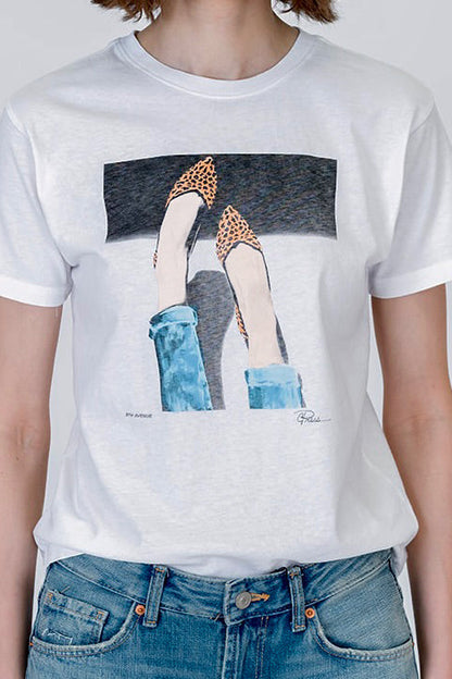 A person wearing a white short-sleeve graphic T-shirt with a stylized "5th Ave" illustration of legs in leopard-print pointed shoes and blue jeans, paired with blue denim jeans, against a light gray studio background.