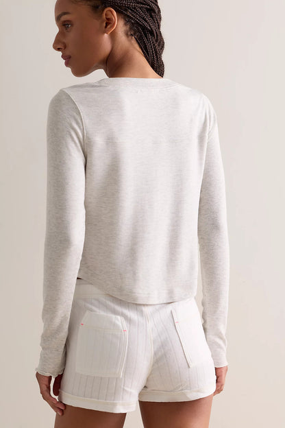 A woman shown from the back wearing a light heather grey long-sleeve cropped top and white shorts against a plain light beige studio background.