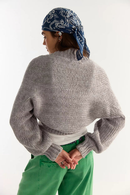 A person shown from the back wearing a chunky gray knit mock-neck sweater, a blue paisley bandana, and green pants against a plain white studio background.