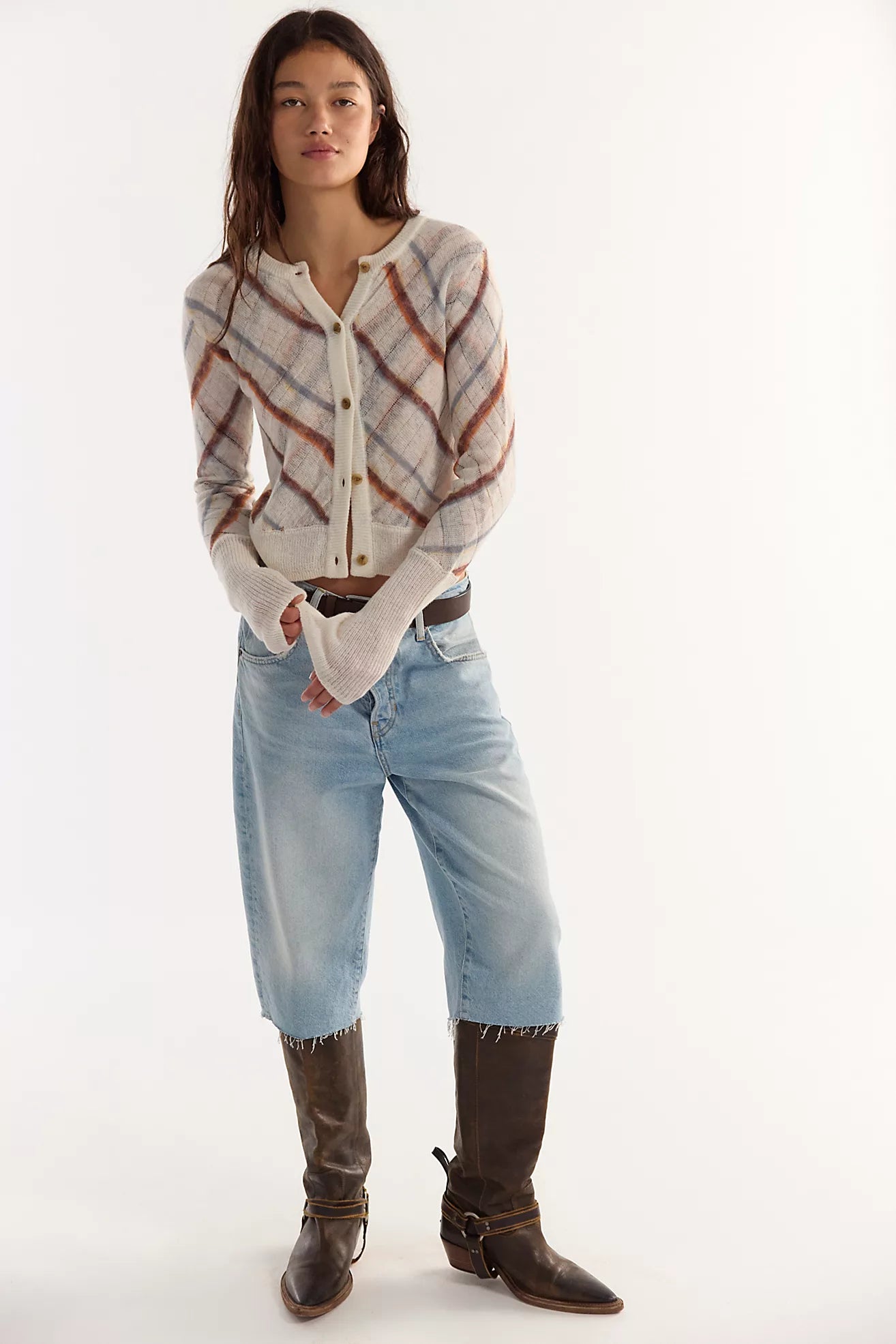 A woman modeling a cream knit cardigan with brown sugar mist combo plaid stripes, paired with light-wash cropped jeans and dark brown leather boots, against a plain white studio background.