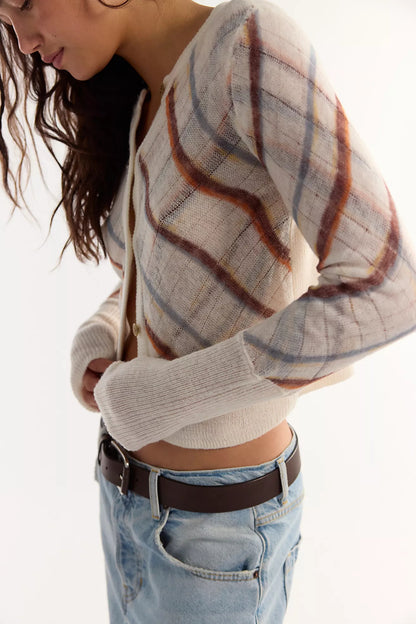 A woman wearing a cropped, long-sleeve knit cardigan with a beige, brown, sugar mist combo plaid pattern, paired with light-wash blue jeans and a dark brown belt, against a plain white background.