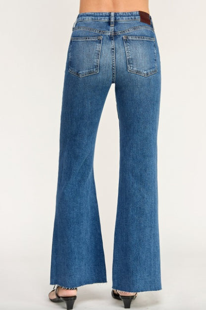 Rear view of a person wearing tulum blue claudia flare jeans with a brown leather waistband patch, shown against a plain light background.