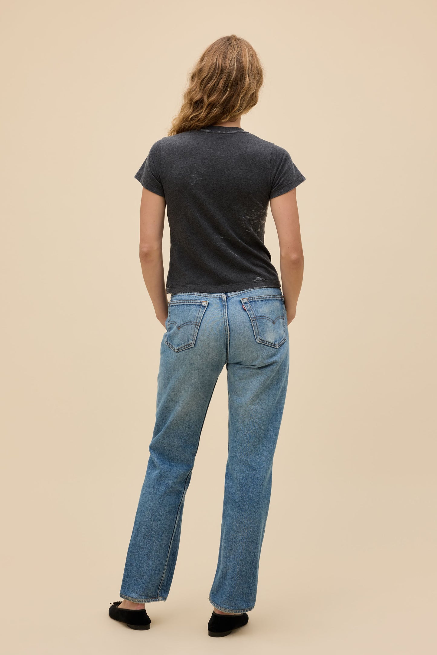 Back view of person wearing a vintage black burnout t-shirt and light blue jeans on a beige background