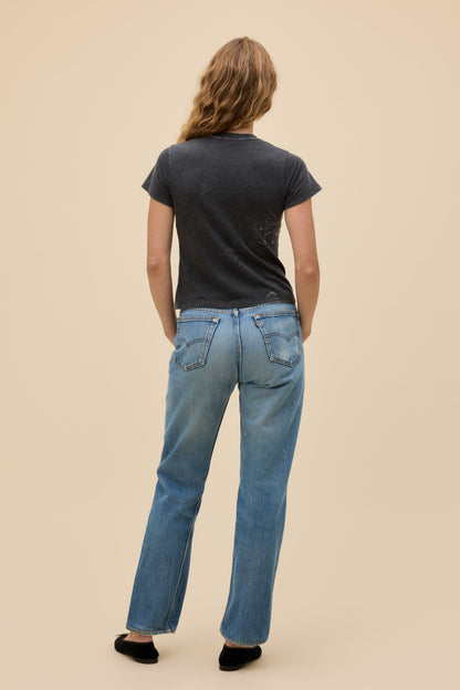 Back view of person wearing a vintage black burnout t-shirt and light blue jeans on a beige background