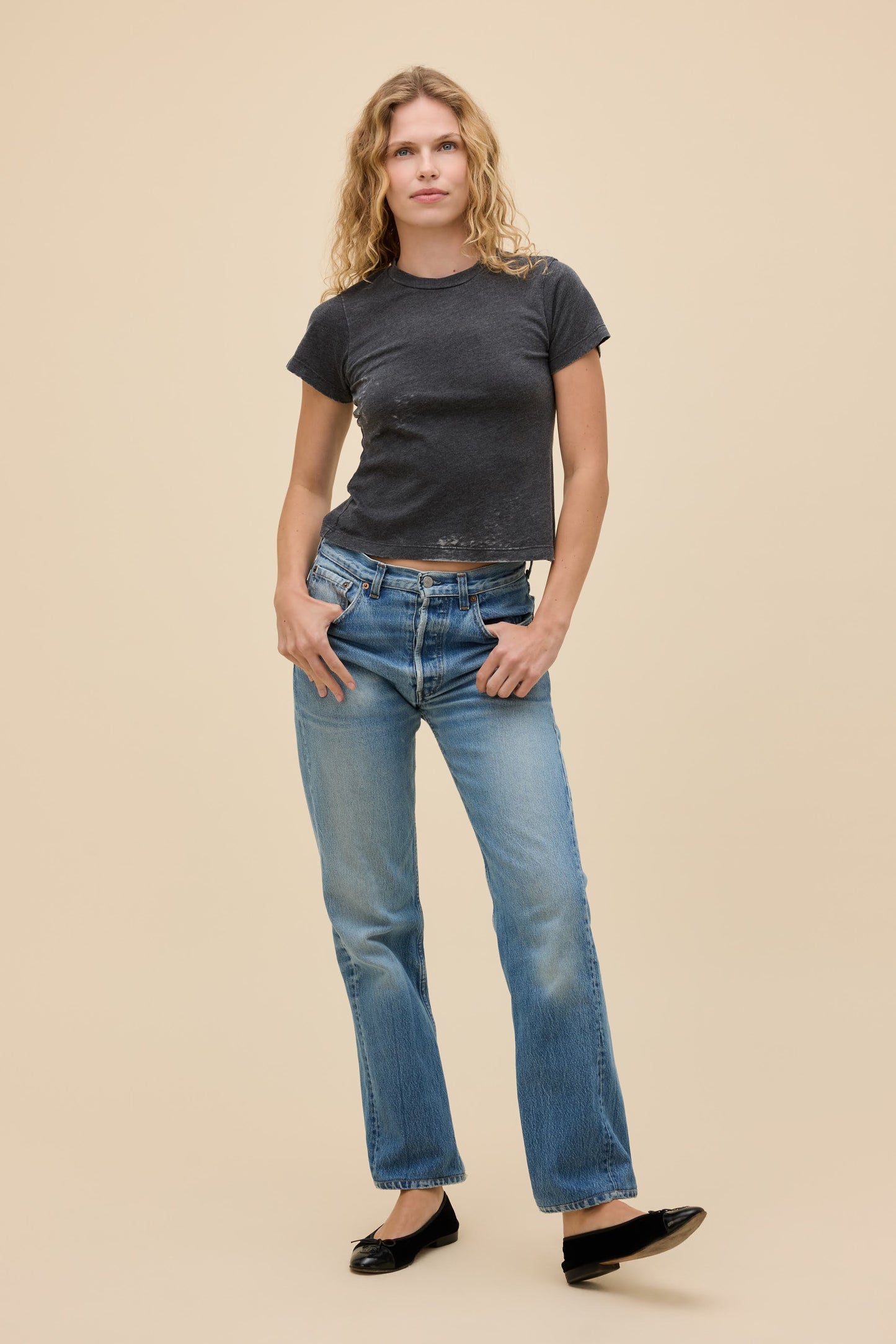Front view of woman wearing a vintage black burnout t-shirt and blue jeans on a beige background