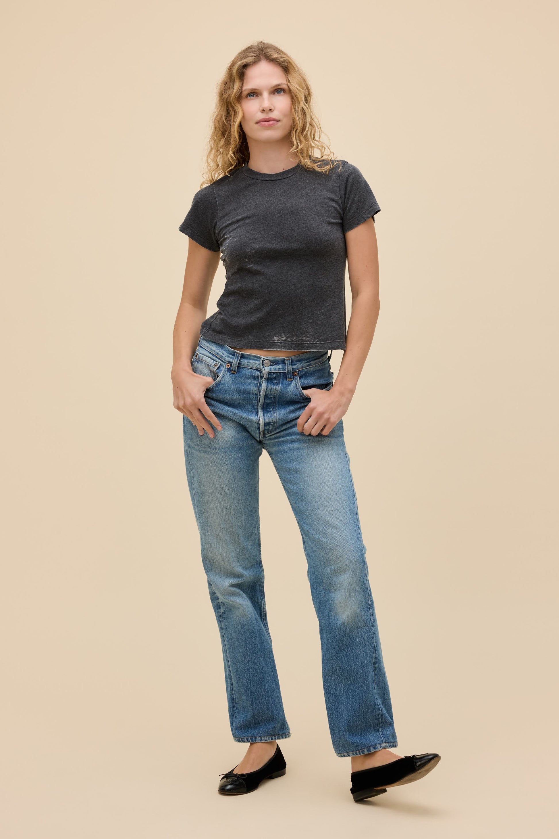 Front view of woman wearing a vintage black burnout t-shirt and blue jeans on a beige background