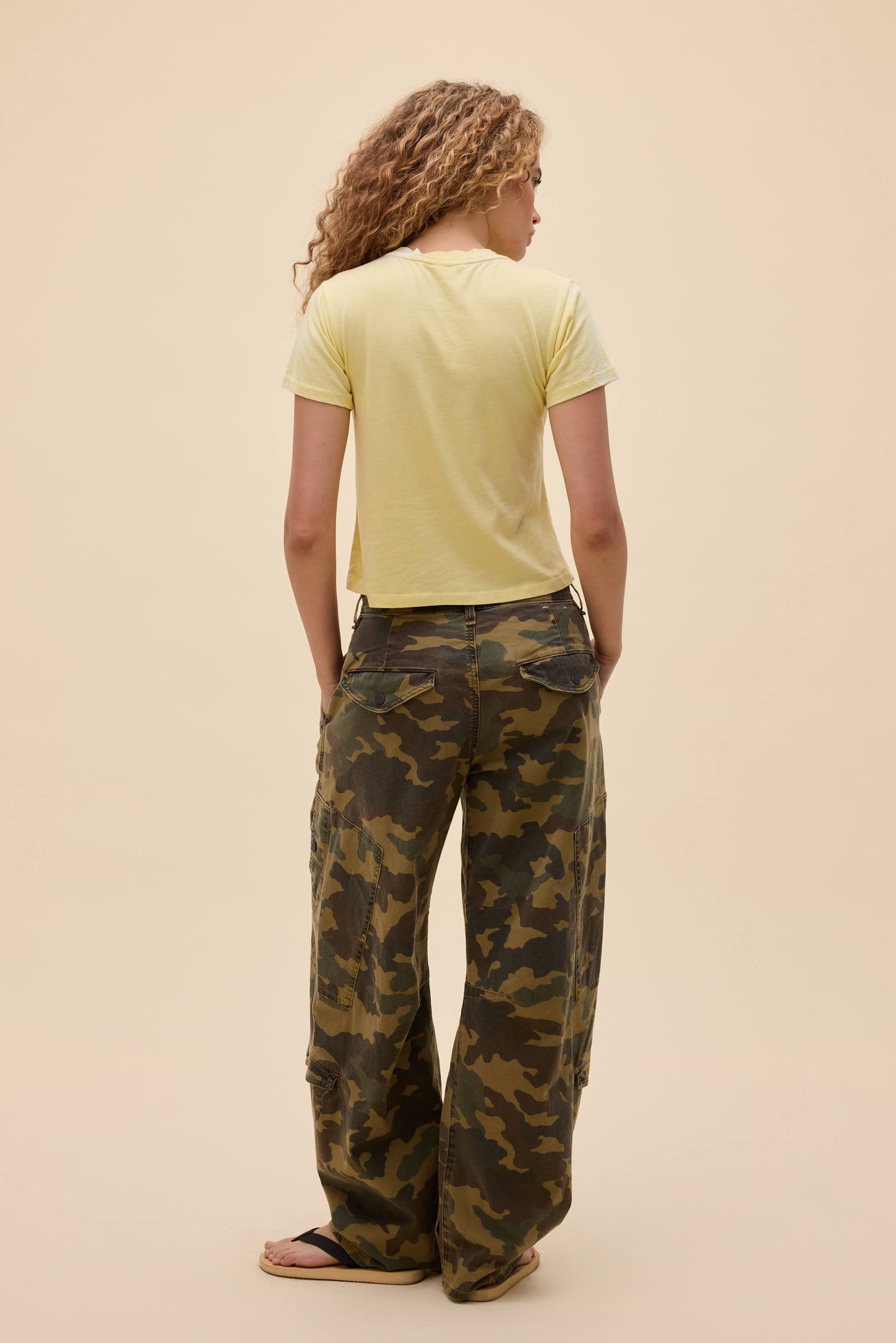 Person wearing a lemon yellow burnout vintage t-shirt and camouflage pants on a beige background