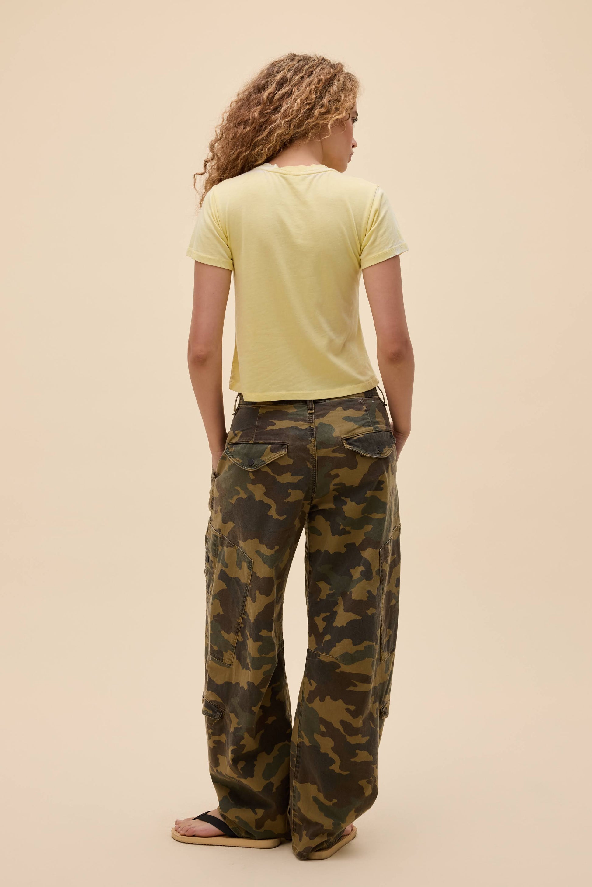 Person wearing a lemon yellow burnout vintage t-shirt and camouflage pants on a beige background