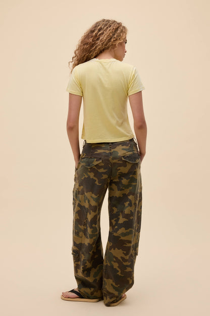 Person wearing a lemon yellow burnout vintage t-shirt and camouflage pants on a beige background