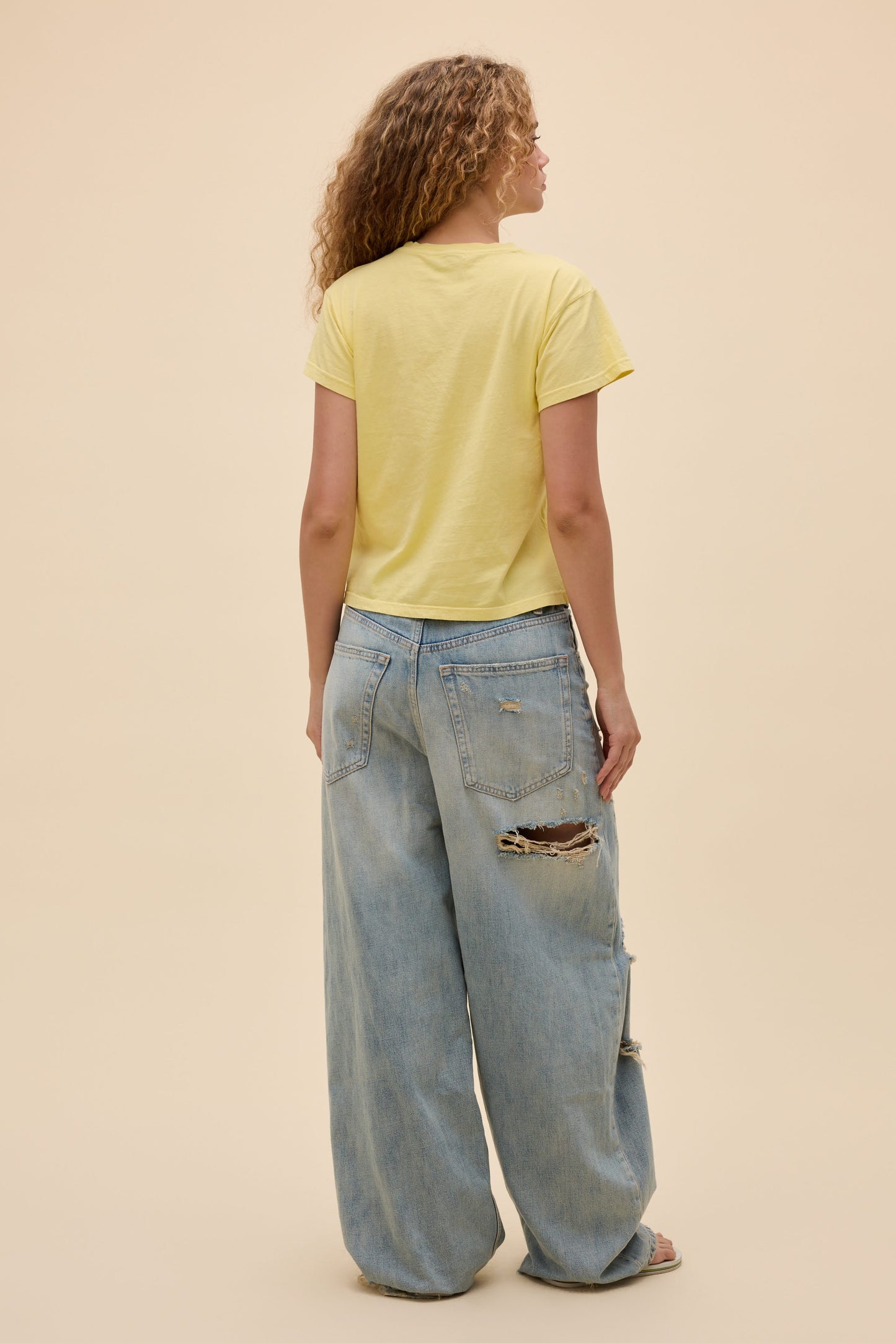 Back view of person wearing a lemon yellow t-shirt and light blue jeans on a beige background