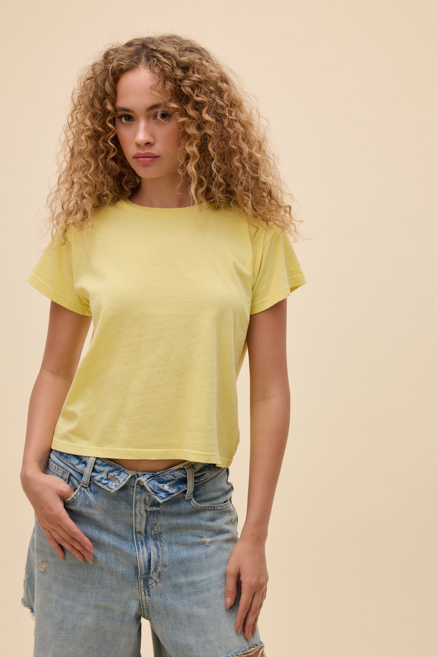 Front view of woman wearing a lemon yellow t-shirt and blue jeans against a beige background