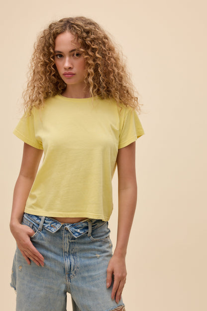 Front view of woman wearing a lemon yellow t-shirt and blue jeans against a beige background