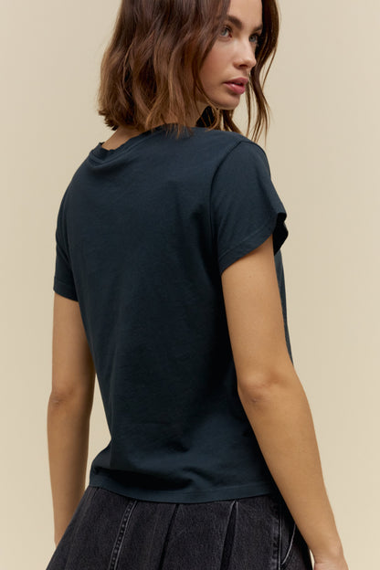 A woman shown from the back wearing a vintage black short-sleeve t-shirt and a dark pleated skirt, set against a plain beige background.