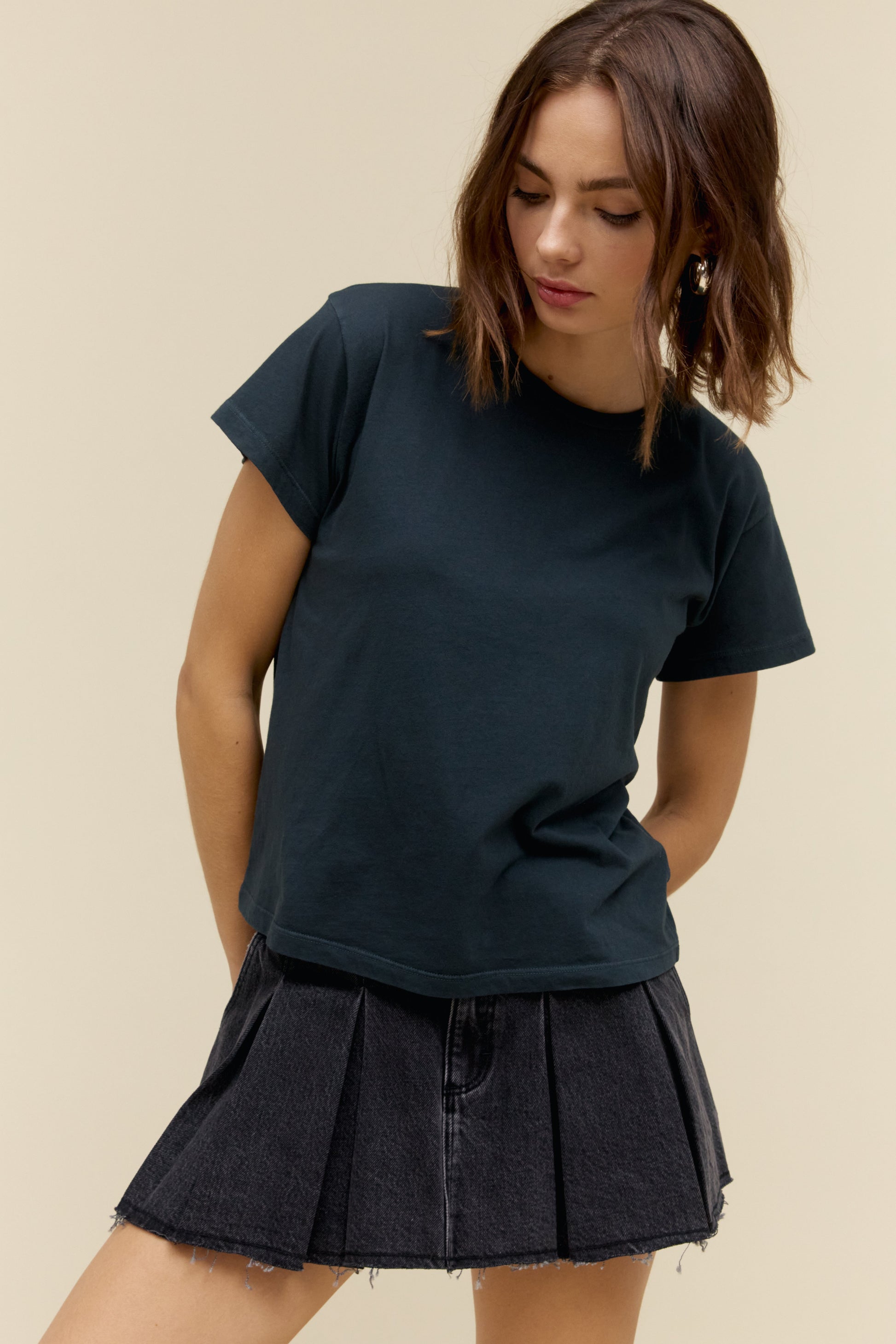 Front view of woman wearing a vintage black t-shirt and black pleated skirt against a beige background