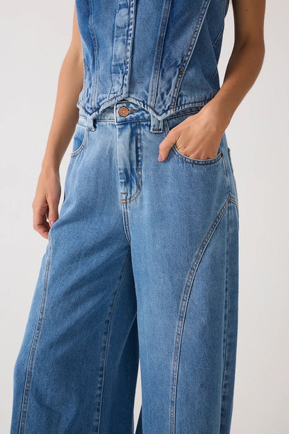 Close-up of a person wearing light blue denim jeans with wide legs, front pockets, and a button closure, against a plain light background.
