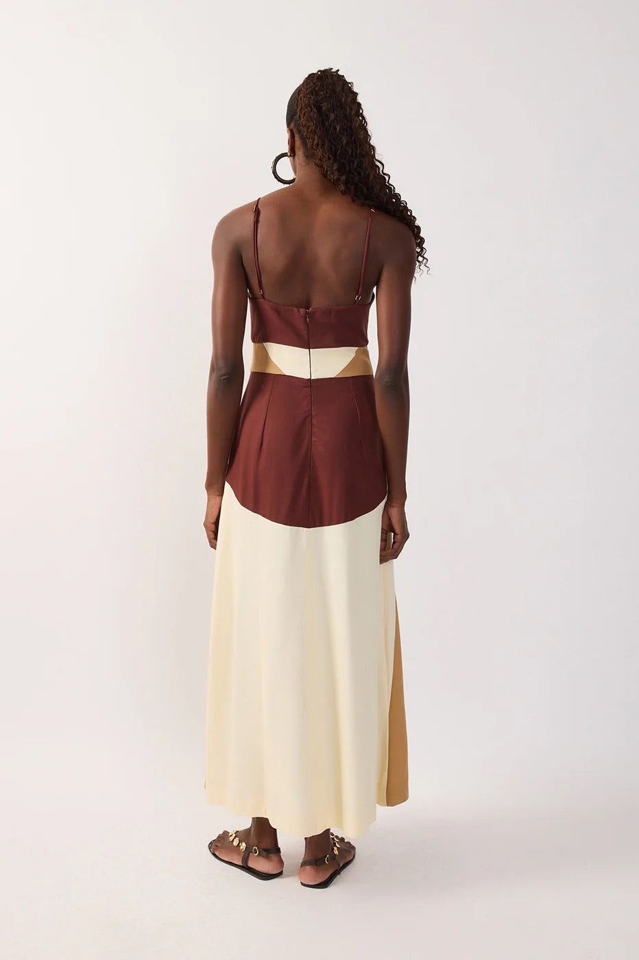 Back view of woman wearing a multicolor-blocked dress with brown, white, and beige sections & a cutout on a white background