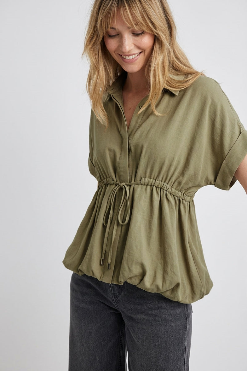 Woman wearing a light olive green bubble hem blouse with a white background