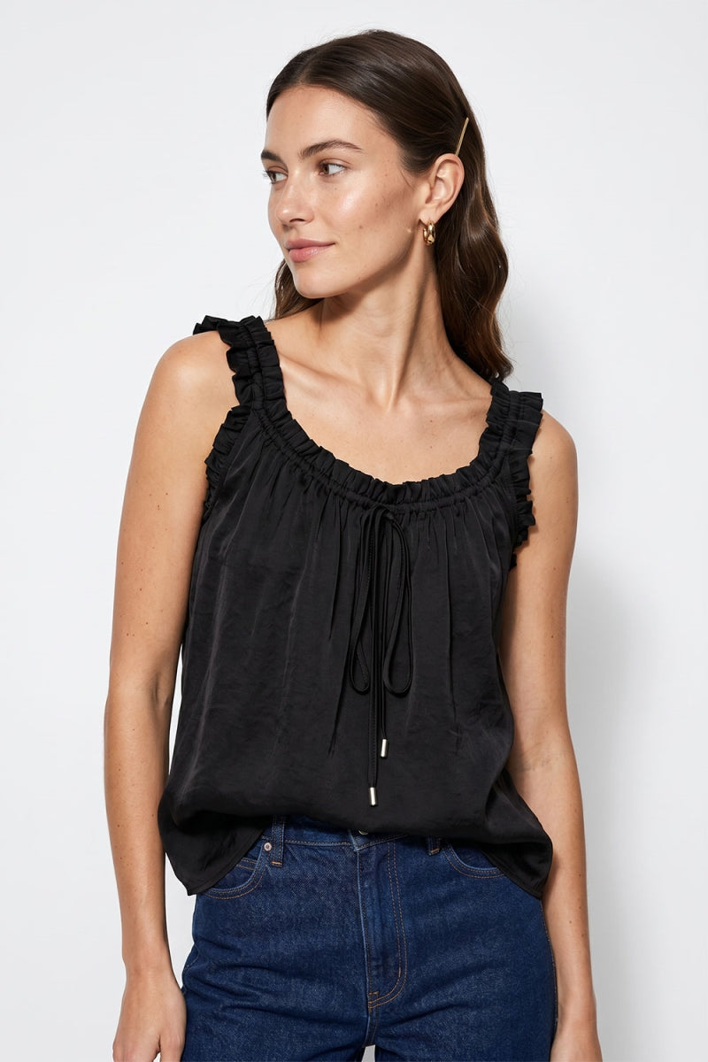 Woman wearing a black sleeveless top with ruffled trim details against a white background