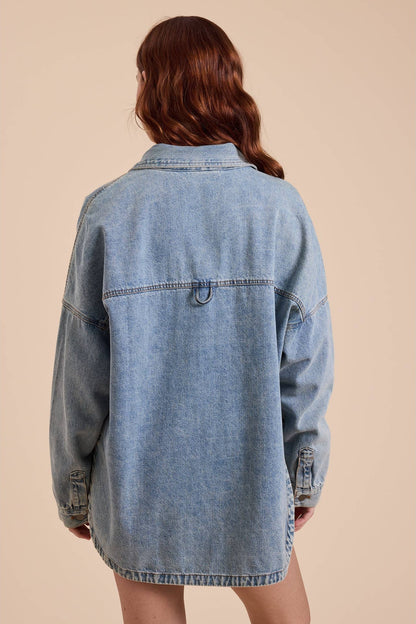 A woman viewed from the back wearing an oversized light-wash blue denim shacket set against a solid beige background.