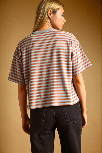 A woman shown from the back wearing a short-sleeve striped crop top with blue and rust horizontal stripes, paired with dark jeans, against a solid warm brown studio background.