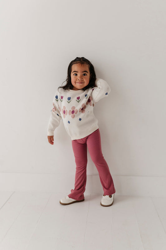 Child wearing a patterned sweater and mesa rose flare pants on a white background