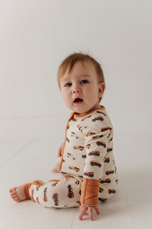 Baby wearing a onesie with pumpkin trucks pattern on a white background