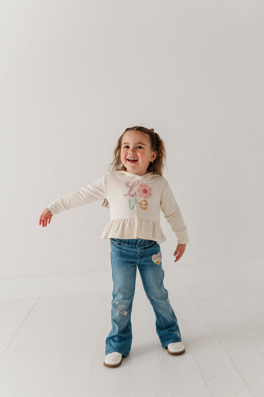Child wearing a white long-sleeve top with floral design and mid wash flare blue jeans on a light background