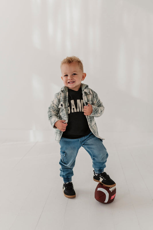 Child wearing a mint plaid shackett and black t-shirt with 'GAME' text, standing on a white background.