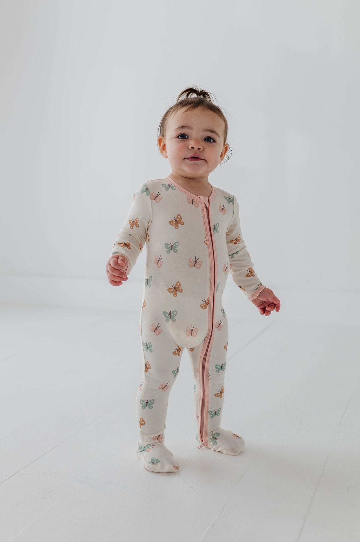 Child wearing a pastel butterflies patterned long-sleeve footie onesie on a plain background