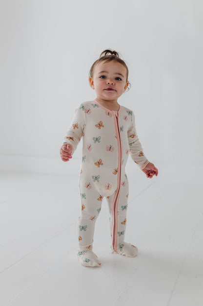 Child wearing a pastel butterflies patterned long-sleeve footie onesie on a plain background