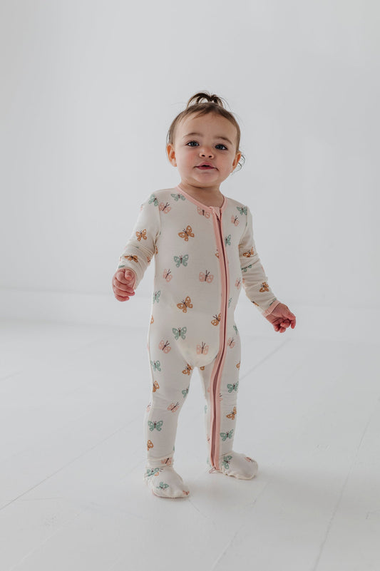 Child wearing a pastel butterflies patterned long-sleeve footie onesie on a plain background