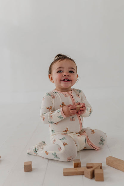 Baby sitting on a white floor with wooden blocks, wearing a pastel butterflies footie romper
