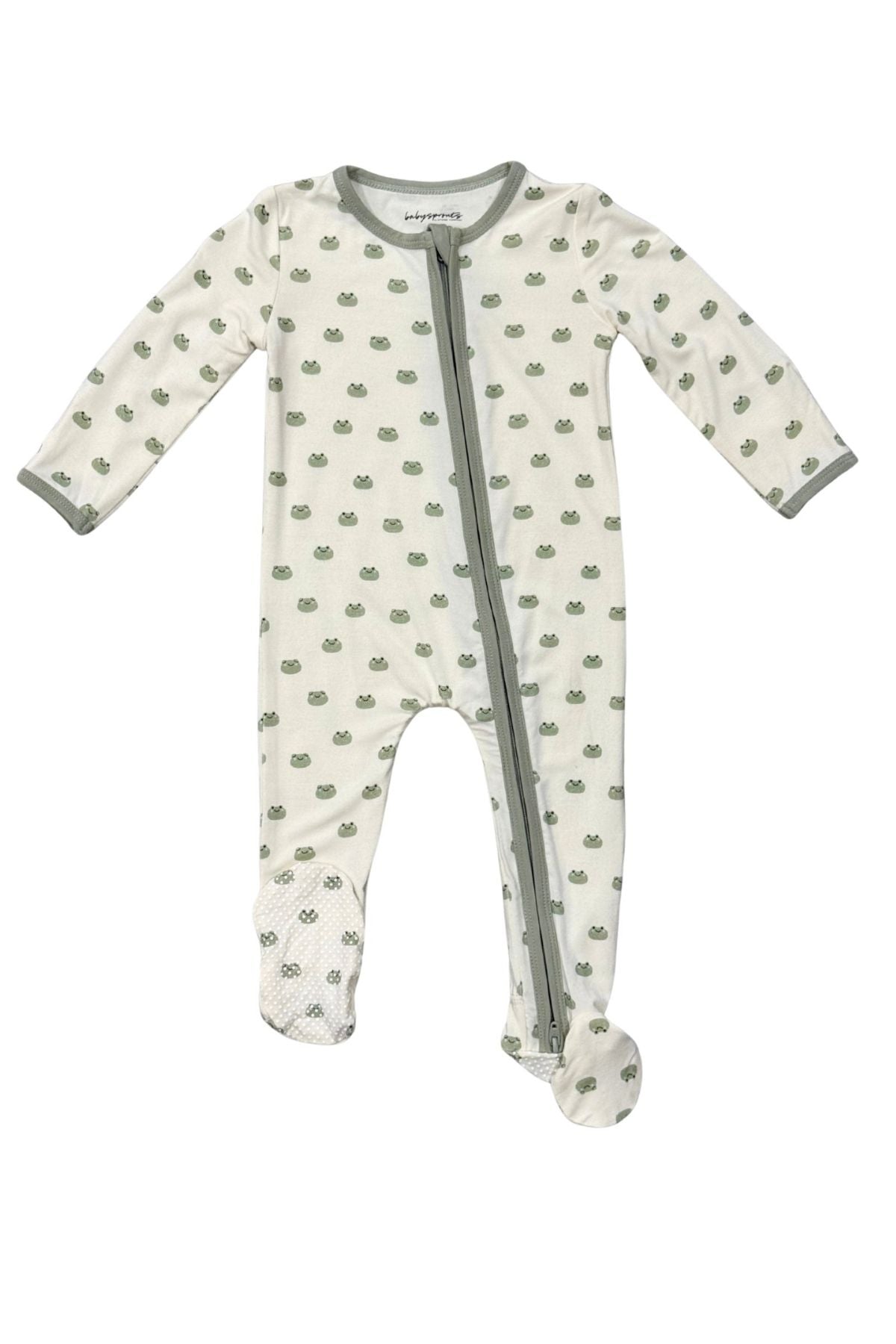 A baby footed sleeper in off-white with a green mini frog pattern and sage green trim, featuring a front zipper.