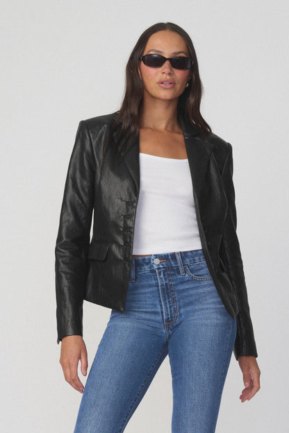Woman wearing black fitted blazer, white shirt underneath, sunglasses, and blue jeans