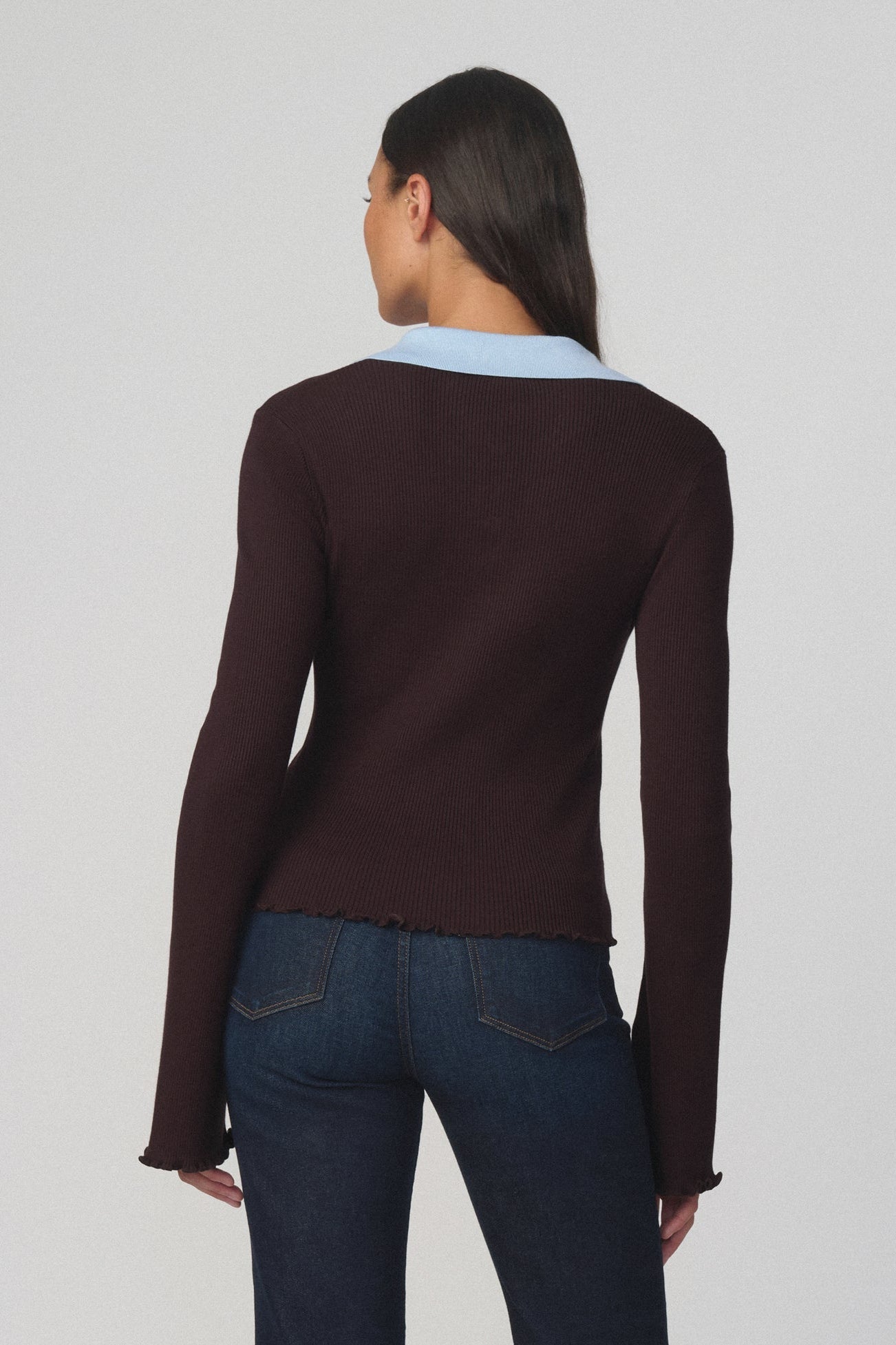 Back view of woman wearing the riley polo sweater in espresso with a light blue collar and dark blue jeans 