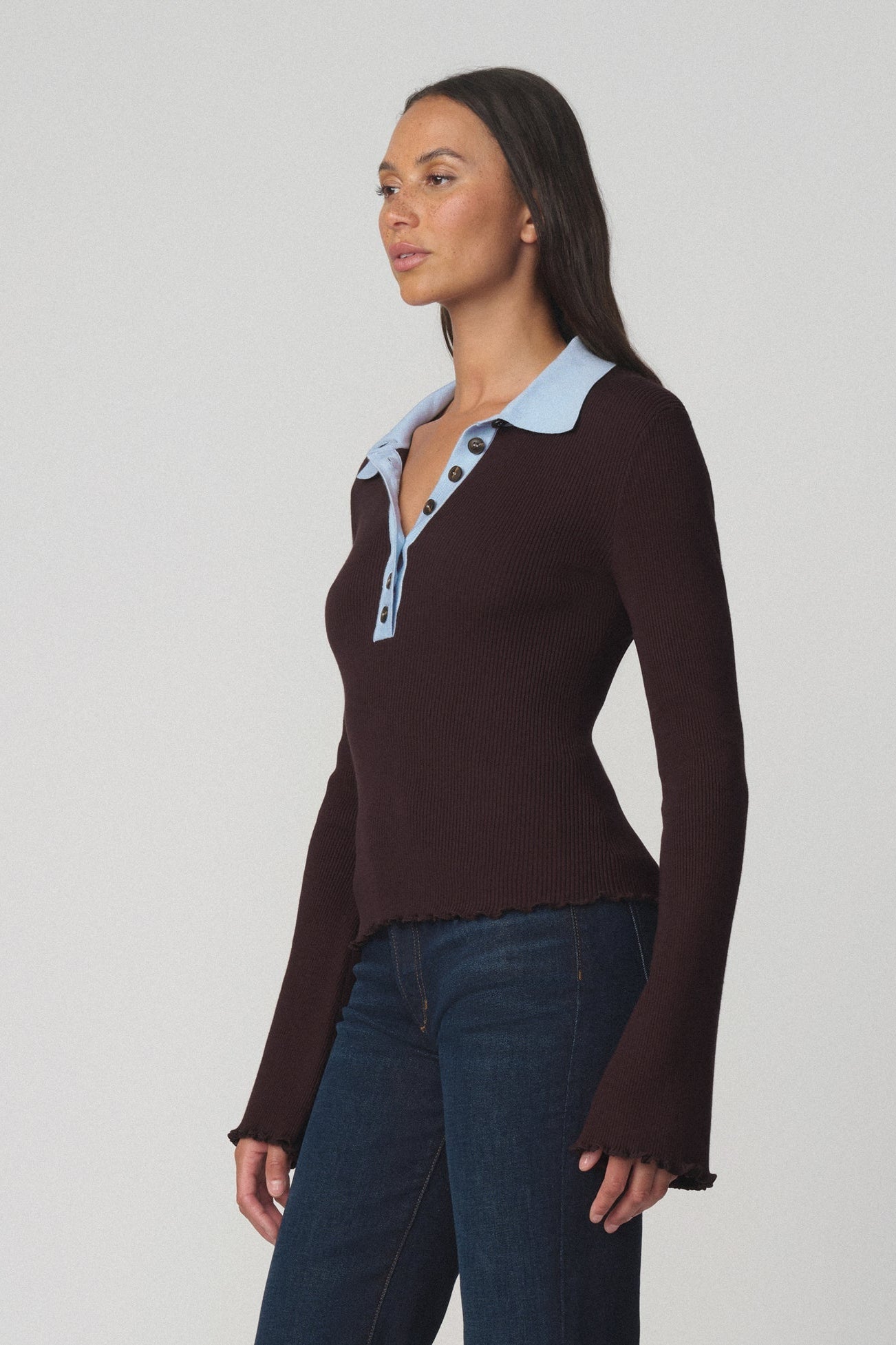 Side view of a woman wearing the riley polo sweater in espresso with a light blue collar and dark blue jeans 